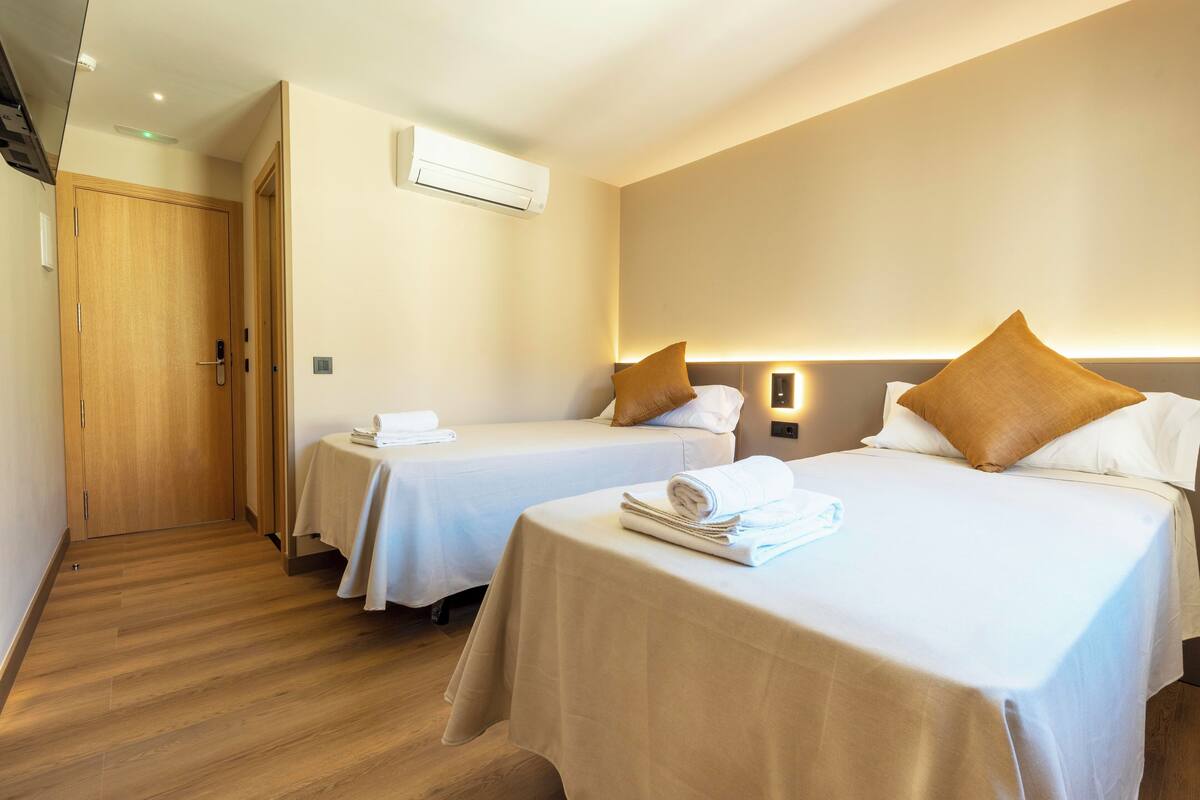 A hotel room with two single beds, a wooden door, an air conditioning unit, and a small table with towels.