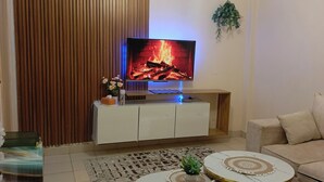 Ein Wohnzimmer mit einem Flachbildfernseher, der einen Kamin zeigt, einem Sofa, einem Couchtisch und einem gemusterten Teppich.