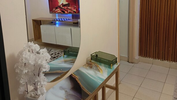 Ein Zimmer mit einem großen Spiegel, einem Fernseher, der ein Feuer zeigt, einem kleinen weißen Schrank und einer Zierpflanze.