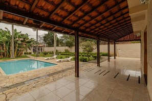 A covered outdoor area with a swimming pool, stone flooring, and lounge chairs. - Ch Cara com Churrasqueira sal o de Jogos e Wi-fi (Suzano)
