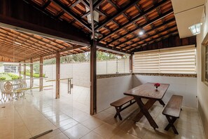 An open patio with a wooden table and benches, tiled flooring, and a view of the outside. - Ch Cara com Churrasqueira sal o de Jogos e Wi-fi (Suzano)