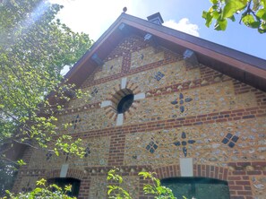 A building with a distinctive brick facade featuring a mosaic of various shapes and sizes. - My Little Normandy   (Notre-Dame-du-Bec)