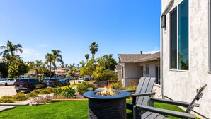 A patio area with a stone fire pit, outdoor seating, and a view of a residential neighborhood. - Airy Ocean Beach Home with Coastal Views (San Diego)