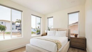 A bedroom with a large bed, a nightstand, and a window with a view of the outside. - Airy Ocean Beach Home with Coastal Views (San Diego)