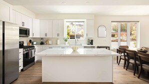 A modern kitchen with white cabinetry, a central island, and a dining area with wooden chairs.