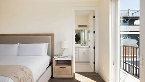 A hotel room with a bed, bedside table, lamp, and a view of the balcony.