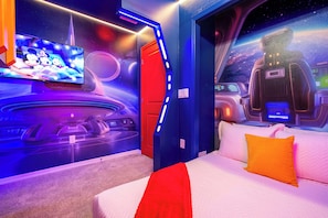 A room with a bed, a TV, and a space-themed mural.