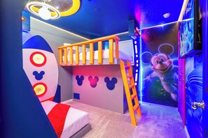Une chambre d’enfant avec un lit superposé, une échelle et une fresque murale représentant Mickey Mouse.
