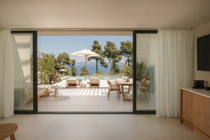 A modern living room with a large sliding glass door leading to a balcony with a pool and outdoor furniture. - Maritima Villas (Kassandra)