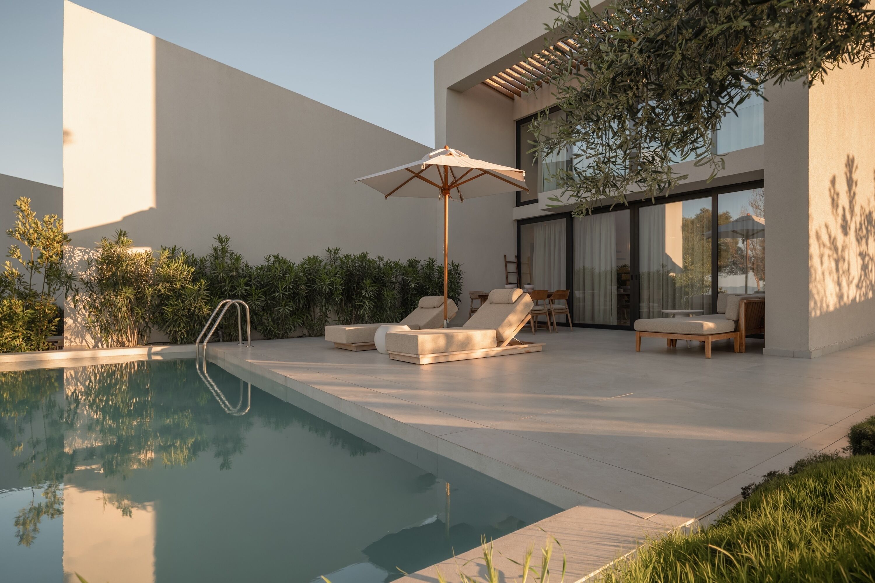 Un espace piscine extérieur moderne, doté de chaises longues, d’une terrasse en bois et d’une pergola.