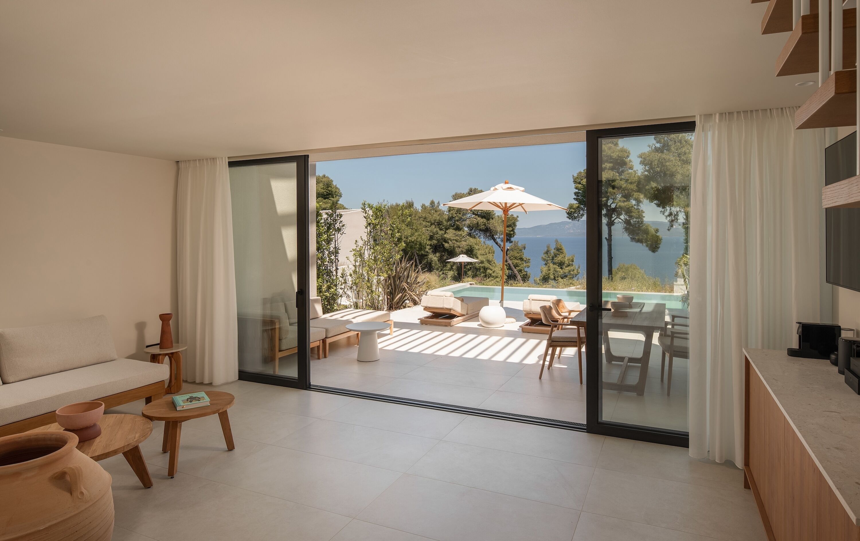 Un salon moderne doté d’une grande porte-fenêtre coulissante donnant accès à un espace piscine aménagé avec du mobilier d’extérieur.
