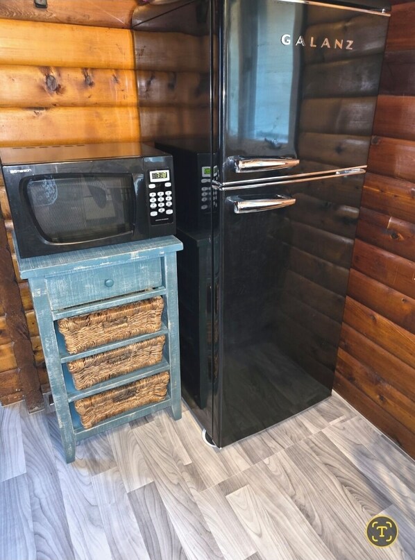 A compact kitchen with a black microwave, a small blue cabinet with wicker baskets, and a black refrigerator labeled "GALANZ".