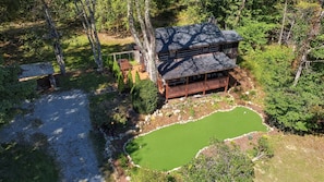 Una cabana de fusta de dos pisos amb terrassa, envoltada per un jardí ben cuidat i un estany petit.