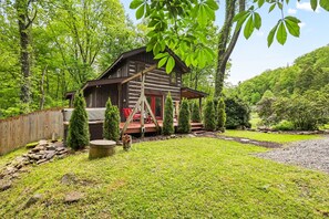 A rustic log cabin with a porch, surrounded by a well-maintained garden and trees.