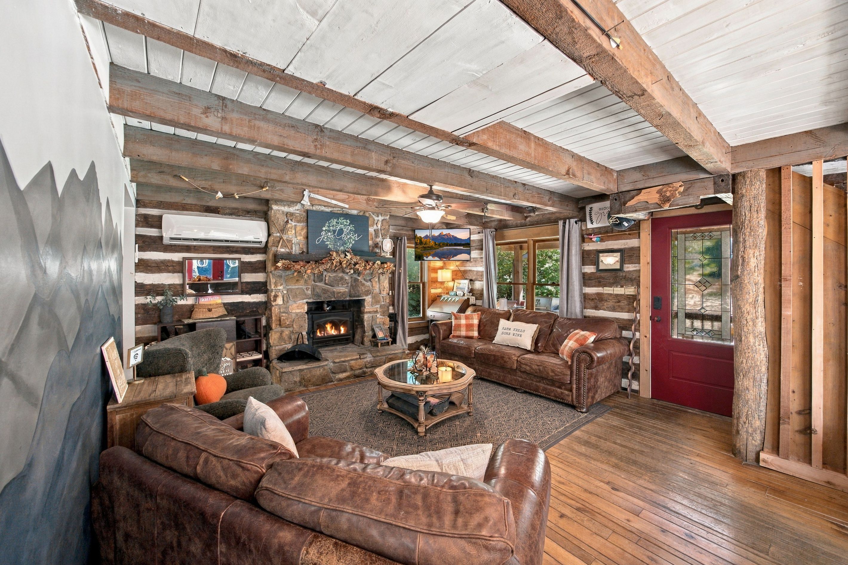 L’intérieur d’un chalet rustique, avec une cheminée en pierre, des canapés en cuir et un plafond en bois.