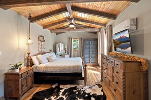 Un dormitorio con techo de madera, una cama, un aparador, un televisor y un tapete de cuero de vaca.