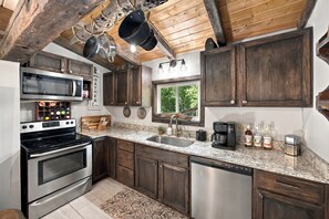 Cocina con armarios de madera, electrodomésticos de acero inoxidable, encimera de granito y ventana con vistas a zonas verdes.