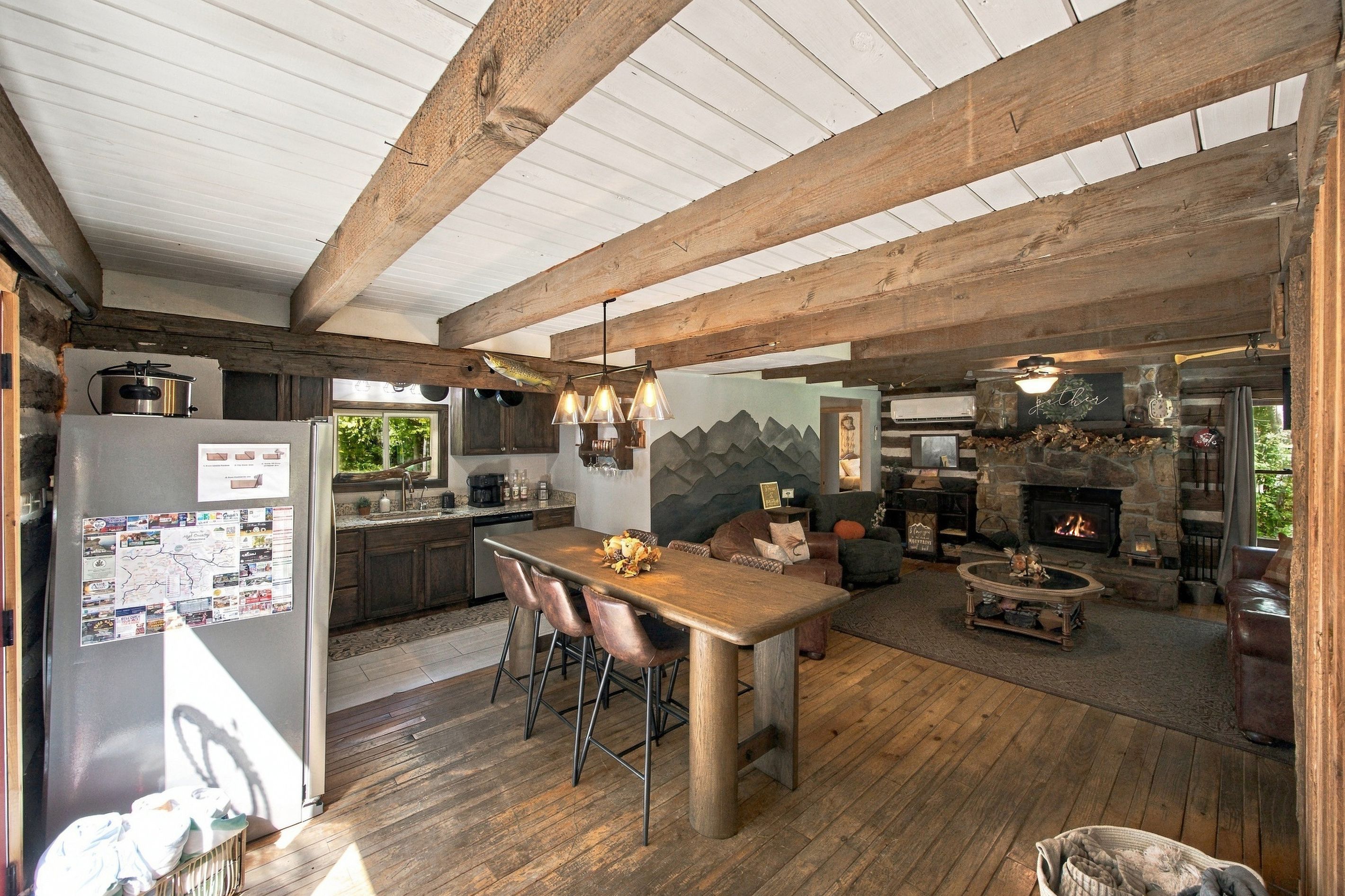 A spacious living area with a wooden floor, a fireplace, and a kitchen with a refrigerator and a stove.