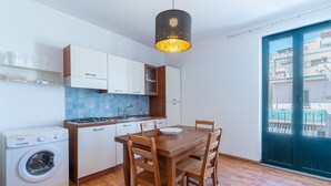 Eine kleine Küche mit Waschmaschine, einem Holzespeisetisch und Stühlen sowie Blick durch eine Schiebetür.