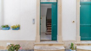Ein Gebäudeeingang mit einer grünen Tür, einer zur Innenseite führenden Treppe und Blumentöpfen an der Wand.