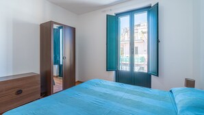 Ein Schlafzimmer mit Bett, Kleiderschrank und einem Fenster mit Blick auf Gebäude.