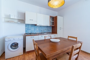 Una cocina compacta con lavadora, una mesa de comedor con sillas y una lámpara colgante.