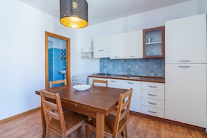 Una cocina compacta con una mesa de comedor de madera, armarios blancos, un salpicadero de azulejos azules y una lámpara colgante.