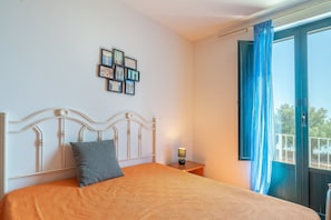 Un dormitorio con cama, mesita de noche, un cuadro en la pared y una ventana con cortinas.