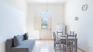 A compact living space with a sofa, dining table, chairs, a refrigerator, and a door leading to an outdoor area. - Apartment 'Terrazza Sul Mare' with Sea View, Wi-Fi and Air Conditioning (Marzamemi)
