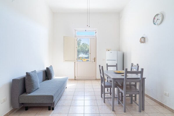 A compact living space with a sofa, dining table, chairs, a refrigerator, and a door leading to an outdoor area.