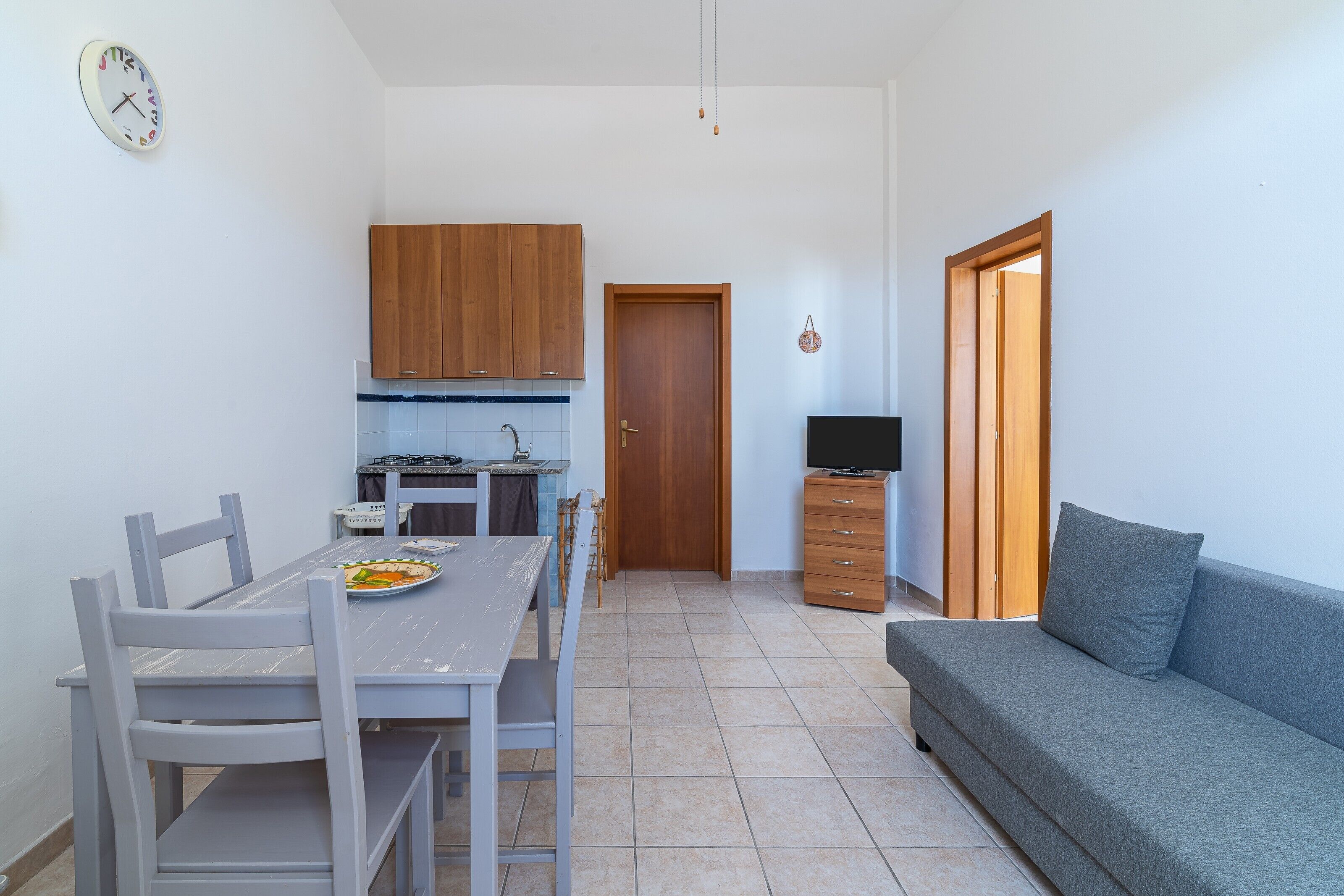 Un ambiente compatto con tavolo da pranzo, sedie, divano, televisione e angolo cottura.