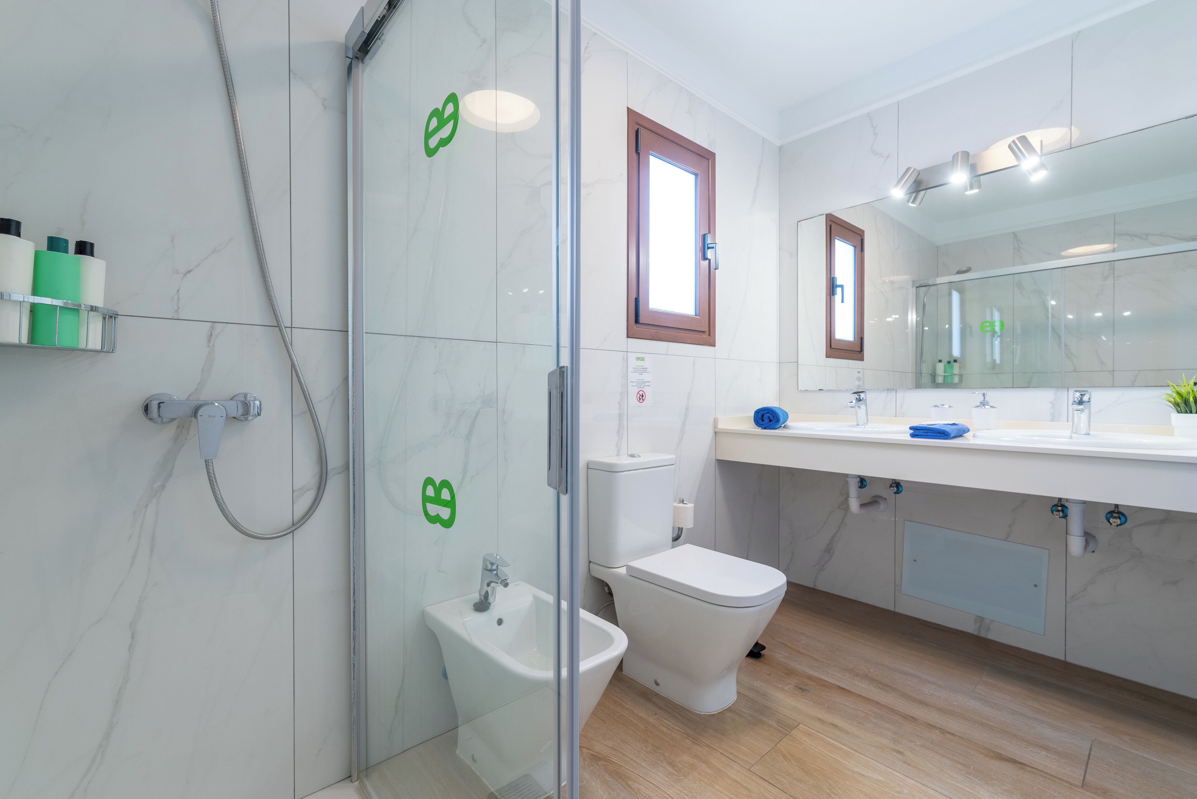 A modern bathroom with a glass shower enclosure, a bidet, a toilet, and a vanity with a mirror.