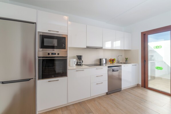 A modern kitchen with white cabinets, a built-in oven, microwave, coffee maker, and dishwasher.