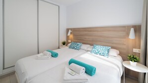 A hotel room with two beds, a wooden headboard, a small bedside table with a lamp, and a potted plant. - Ereza Villas La Granja (Yaiza)