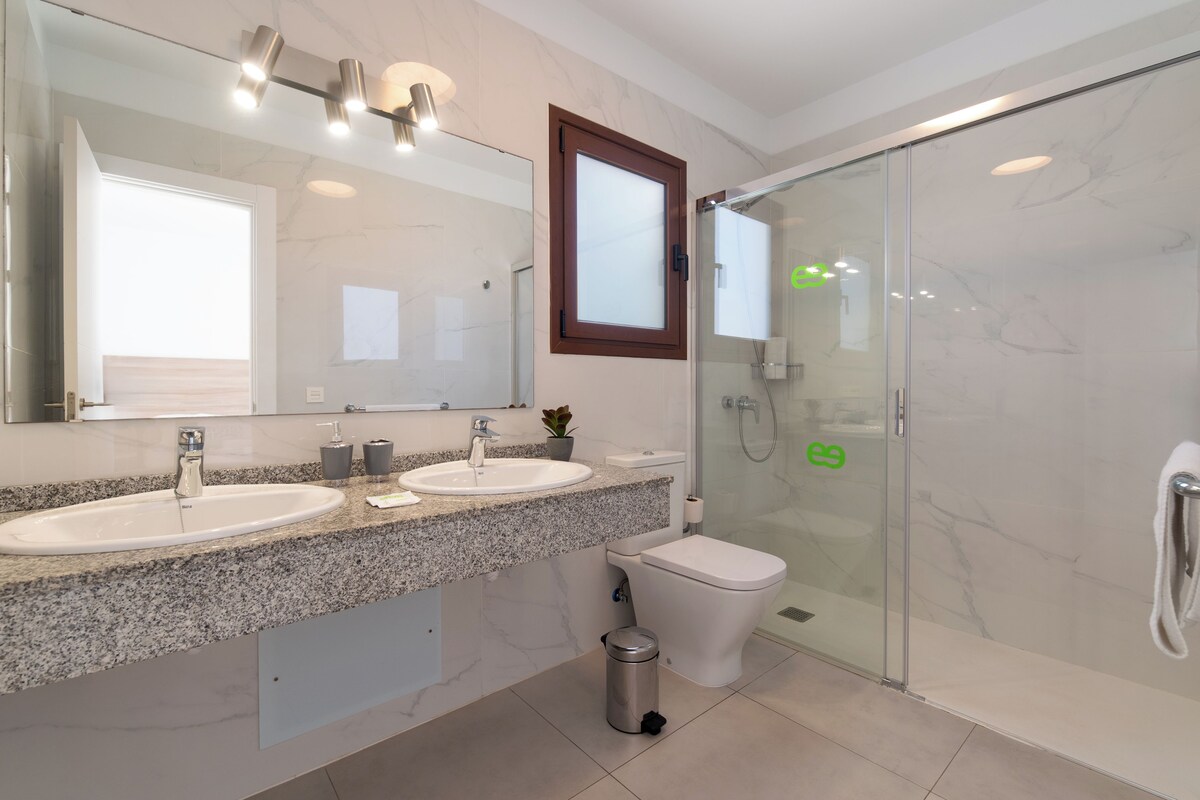 Ein modernes Badezimmer mit zwei Waschbecken, einer Toilette und einer Duschkabine aus Glas.