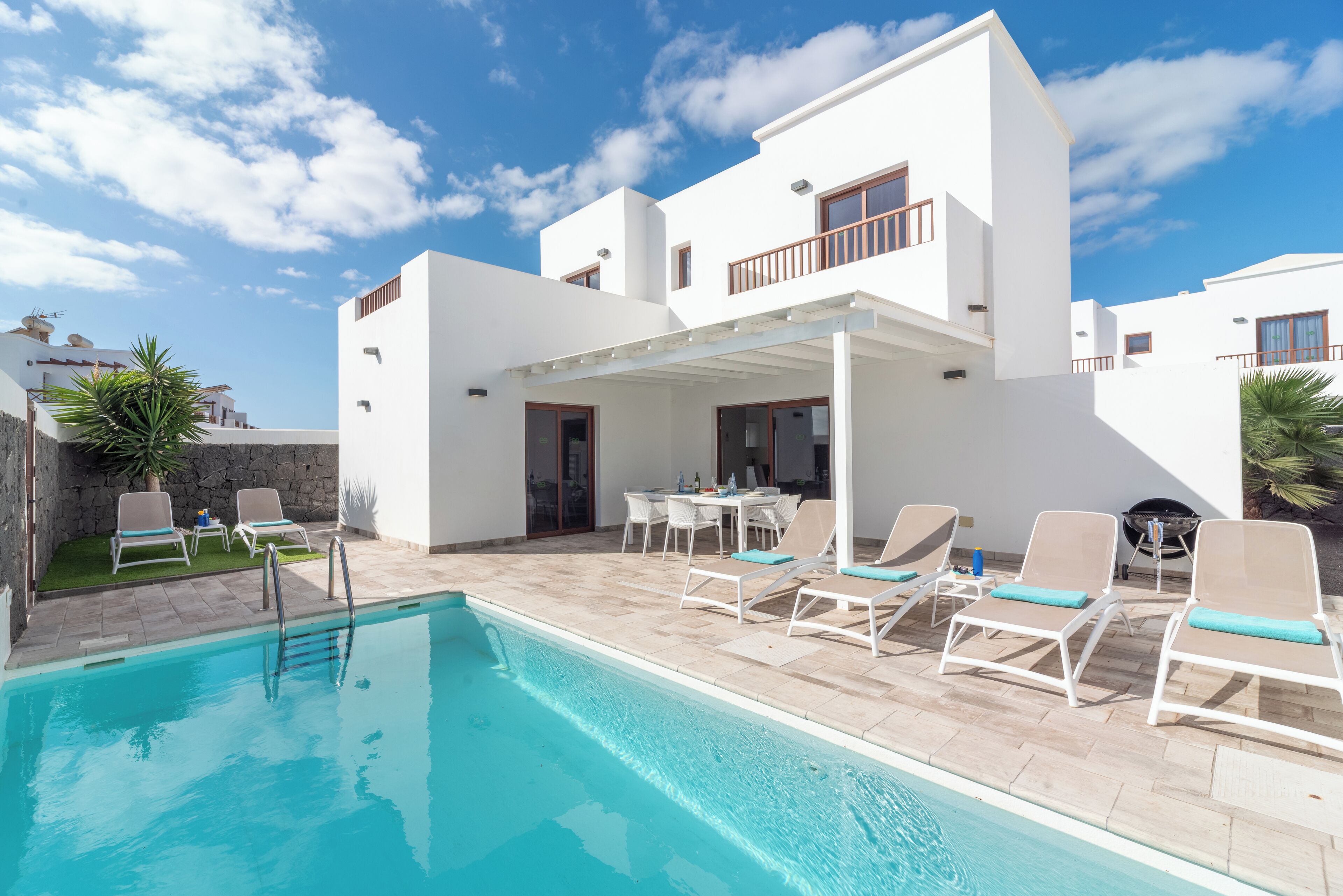 A modern white building with a swimming pool, outdoor seating, and a covered patio area.