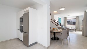 A modern kitchen with a built-in oven and refrigerator, a dining area with a table and chairs, and a staircase leading to another level. - Ereza Villas La Granja (Yaiza)