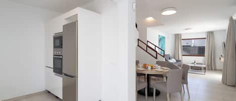 Una cocina moderna con horno y refrigerador integrados, un comedor con mesa y sillas, y una escalera que conduce a otro nivel.