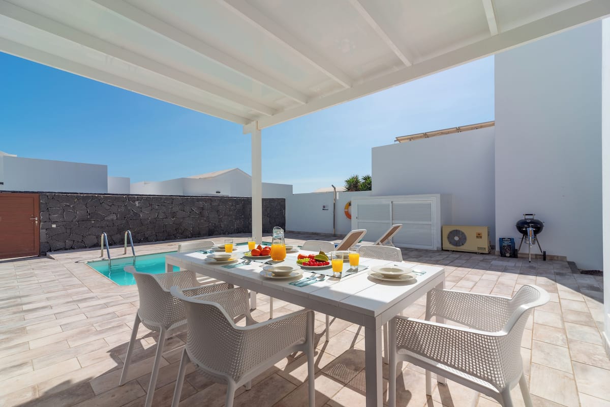 An outdoor patio with a pool, dining table set for four, and a barbecue grill.