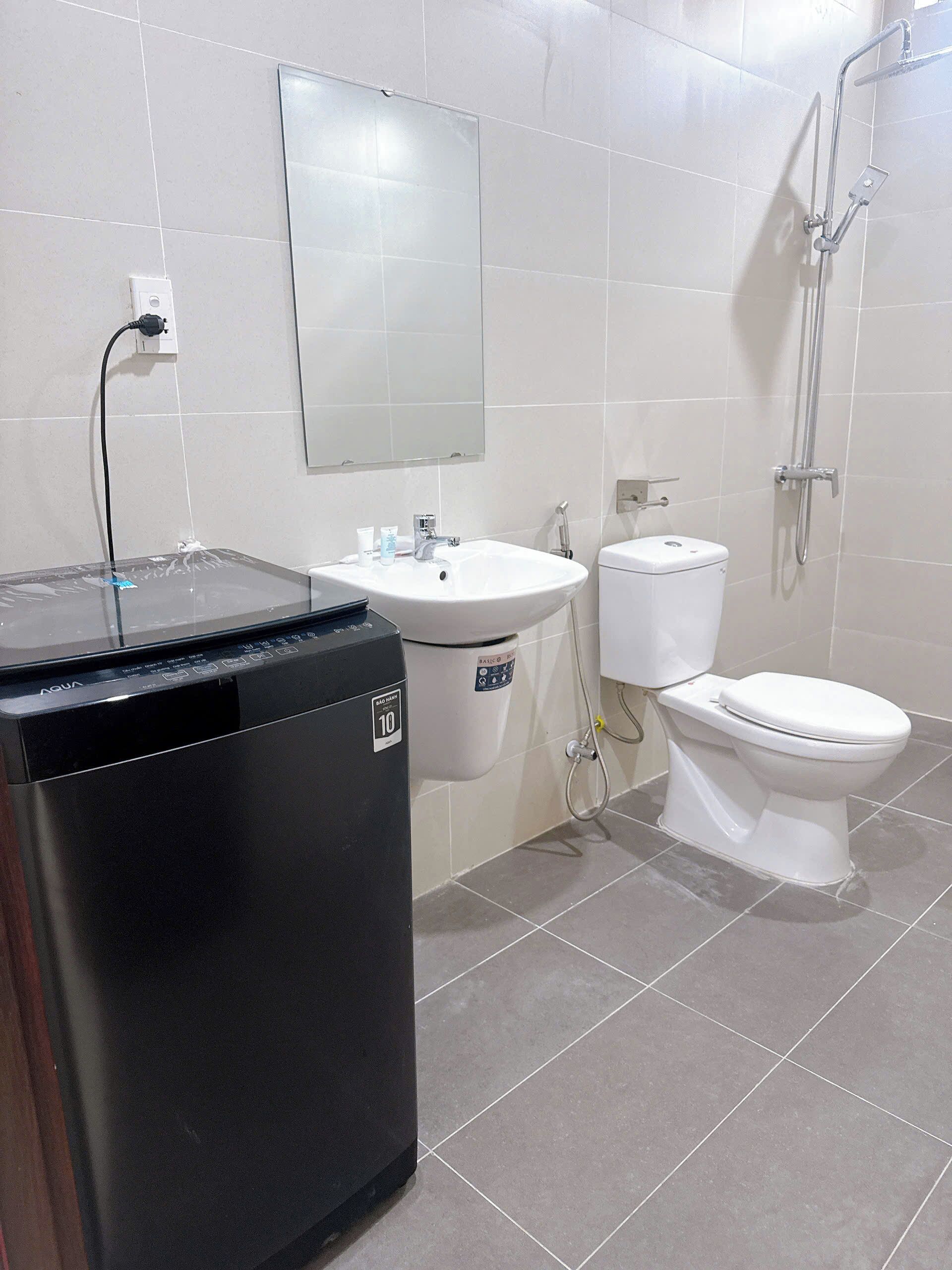 A bathroom with a black washing machine, a white sink, a toilet, and a shower.