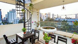 A rooftop terrace with a spiral staircase, wooden furniture, potted plants, and a large planter. - LOUIS OTIS APARTMENT 03 (Da Nang)