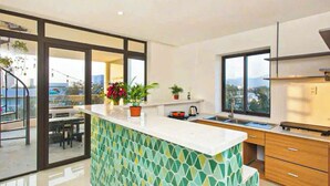 A modern kitchen with a large island, a dining area with a view, and a staircase leading to an outdoor balcony. - LOUIS OTIS APARTMENT 03 (Da Nang)