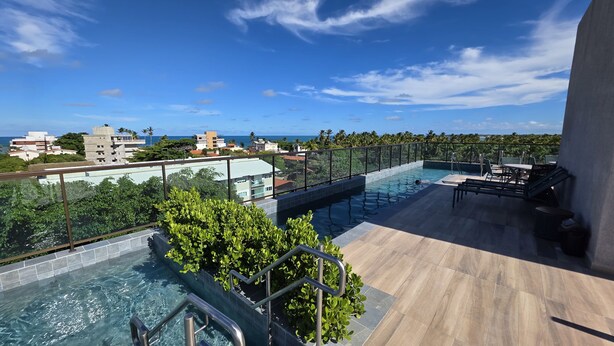 A rooftop pool area with a view of the ocean and surrounding buildings. - Flat Centro Porto de Galinhas 204 byLP (Ipojuca)
