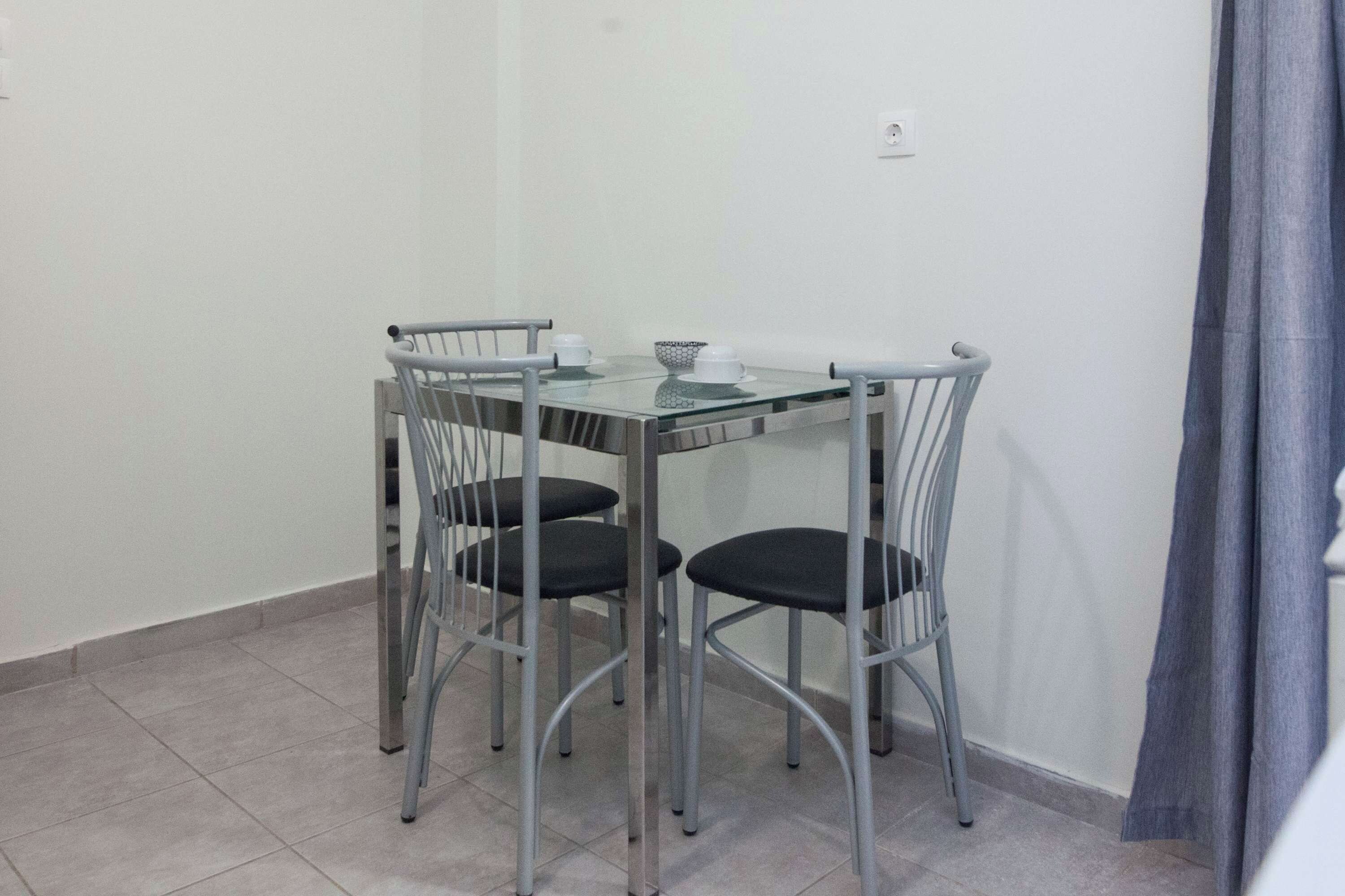 A small, modern dining area with a glass-top table and four metal chairs.