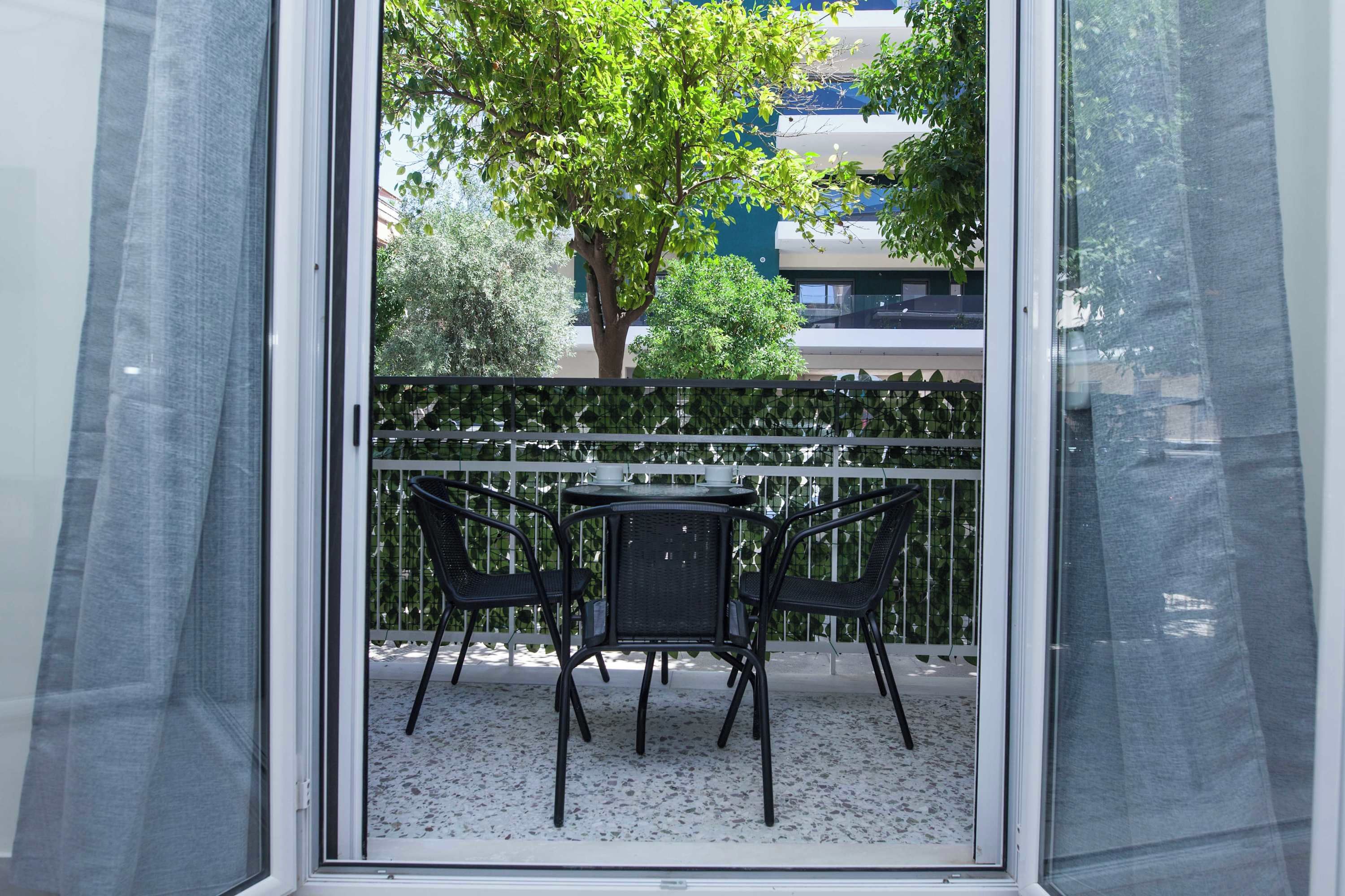 A balcony with a table and chairs, a white railing, and a view of trees and buildings.