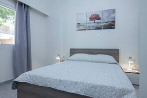 Una cama bien hecha con una colcha blanca estampada, un cabecero de madera y dos lámparas de noche sobre una mesita.