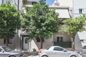 Vista callejera con coches aparcados, árboles y un edificio de fachada blanca y una puerta.