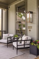 A porch with two chairs, a small table, a potted plant, and a mailbox.