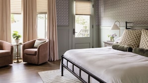 Una camera da letto con un letto, una sedia, un comodino, una lampada e una porta.