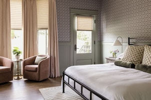 A bedroom with a bed, a chair, a bedside table, a lamp, and a door.